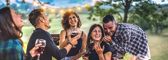 Leute sitzen in Abendlicht draußen und trinken Rotwein