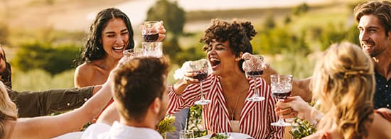 Menschen sitzen draußen an Tisch, lachen und trinken Rotwein