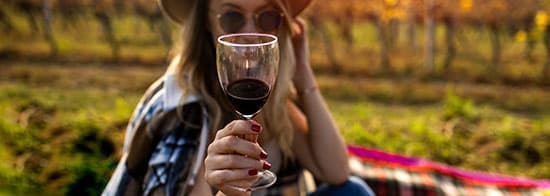 Frau mit Hut hält Rotweinglas in Kamera