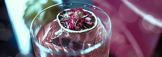 Glas mit lila Flüssigkeit und Blüte