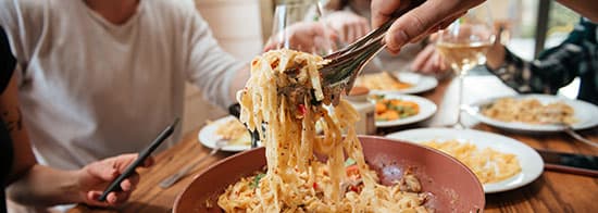 Weißweingläsern und Pasta in Tellern auf Tisch