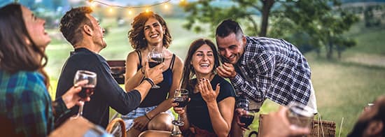 Leute sitzen in Abendlicht draußen und trinken Rotwein