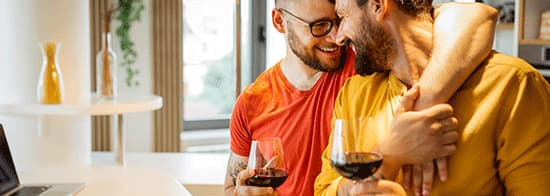 Zwei Männer umarmen sich in Küche und trinken Rotwein