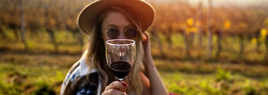 Frau mit Hut und Sonnenbrille hält Rotweinglas