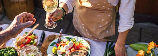 Frau steht an Tisch und bietet Weißwein mit Salat an