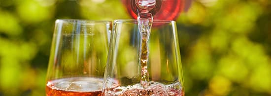 Hand füllt Roséwein in Glas aus Roséweinflasche 
