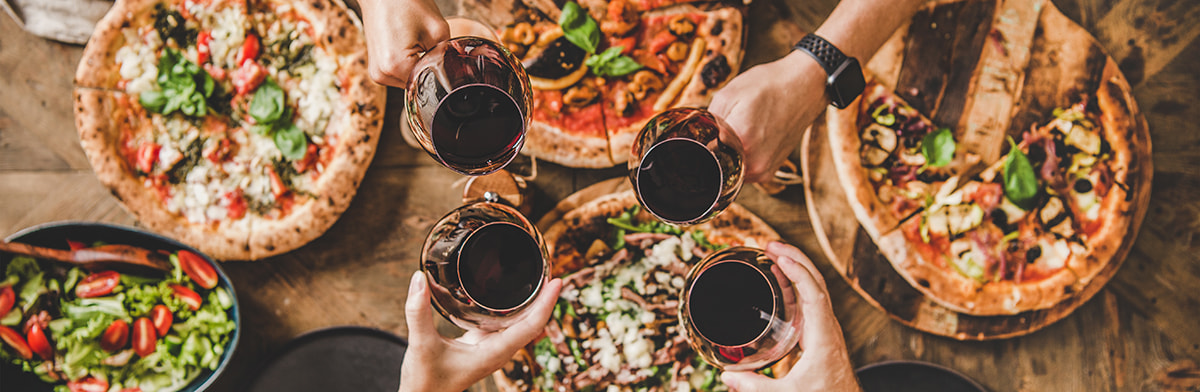 Gedeckter Tisch mit Pizza und Leute, die mit Rotwein anstoßen