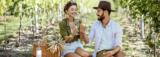 Lachendes Paar sitzt zwischen Reben und trinkt Weißwein