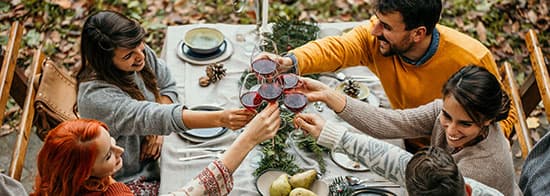 Menschen an Tisch lachen und stoßen mit Rotwein an