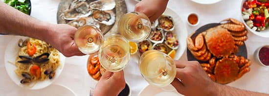 Menschen trinken Weißwein an gedeckten Tisch mit Fisch