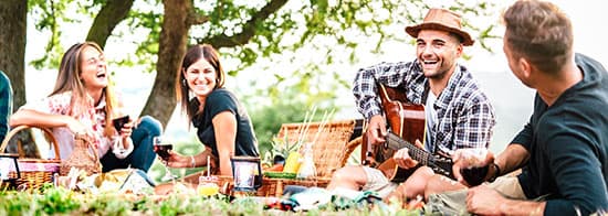 Junge Menschen sitzen auf Wiese, spielen Gitarre und trinken Wein