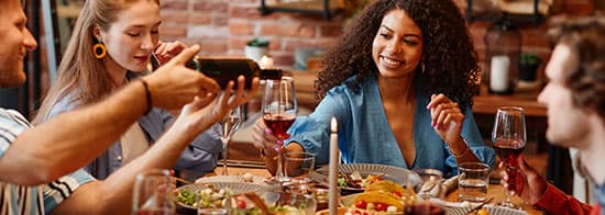 Menschen sitzen an Essentisch und trinken Wein